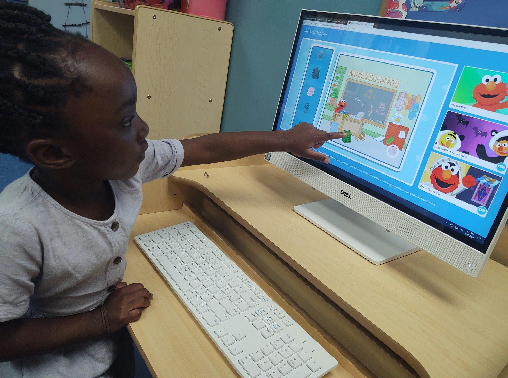 Child pointing at a computer screen showing educational content