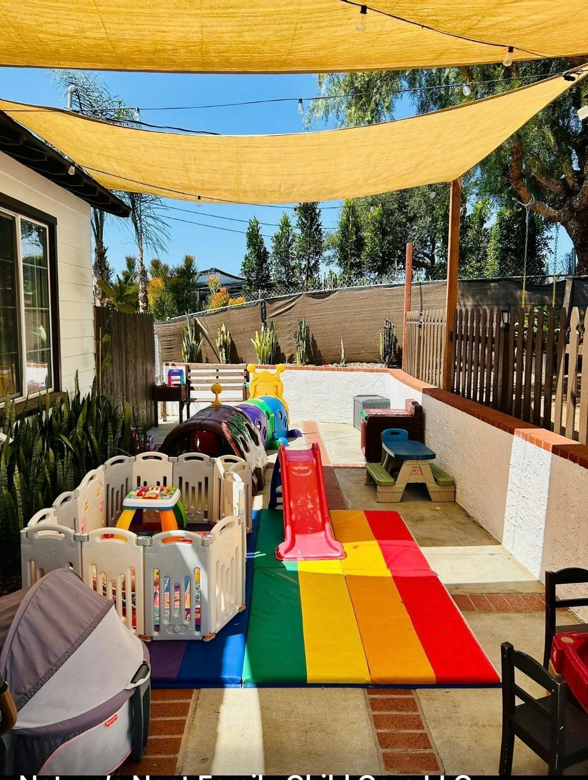 Outdoor children play area with plastic slide and playpen under a sun shade