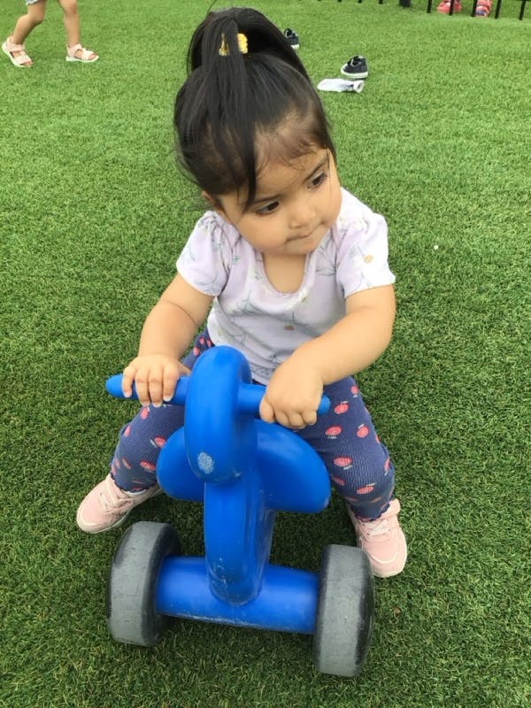 Child riding a blue toy motorcycle on green artificial grass