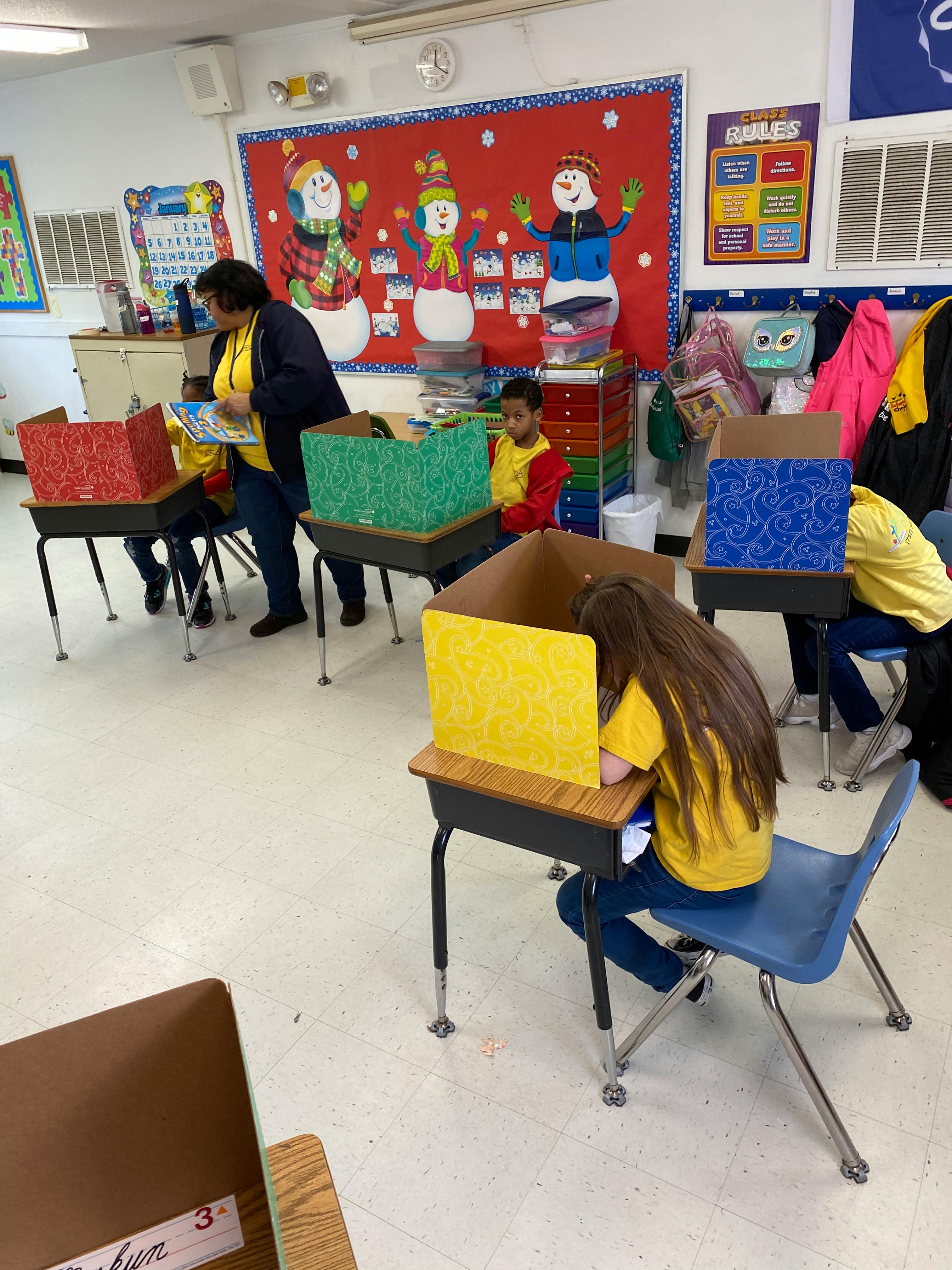 Adult and children in a classroom with privacy shields on desks