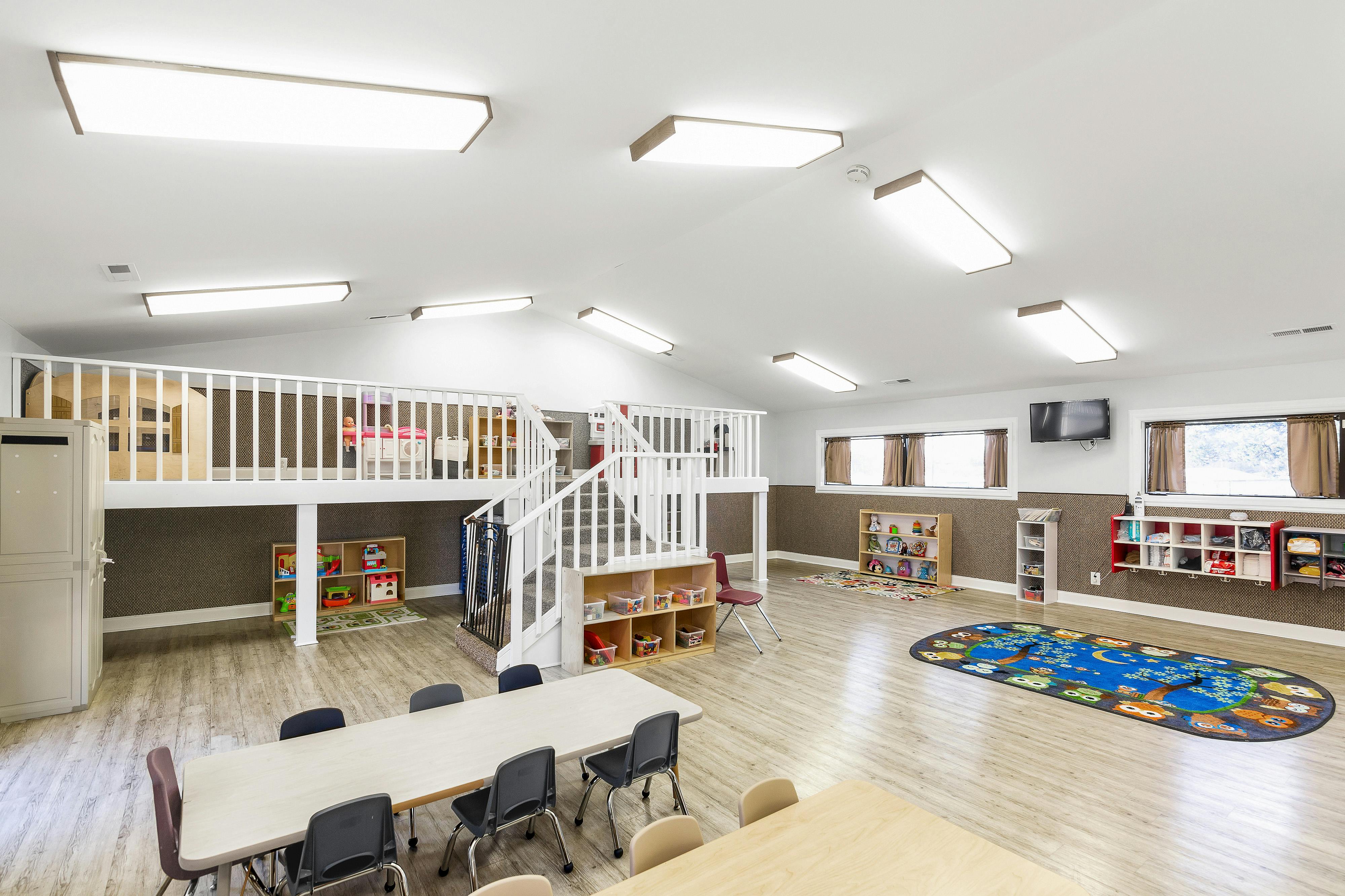 Playroom with multiple tables and chairs, a two-story play structure, and children's cubbies