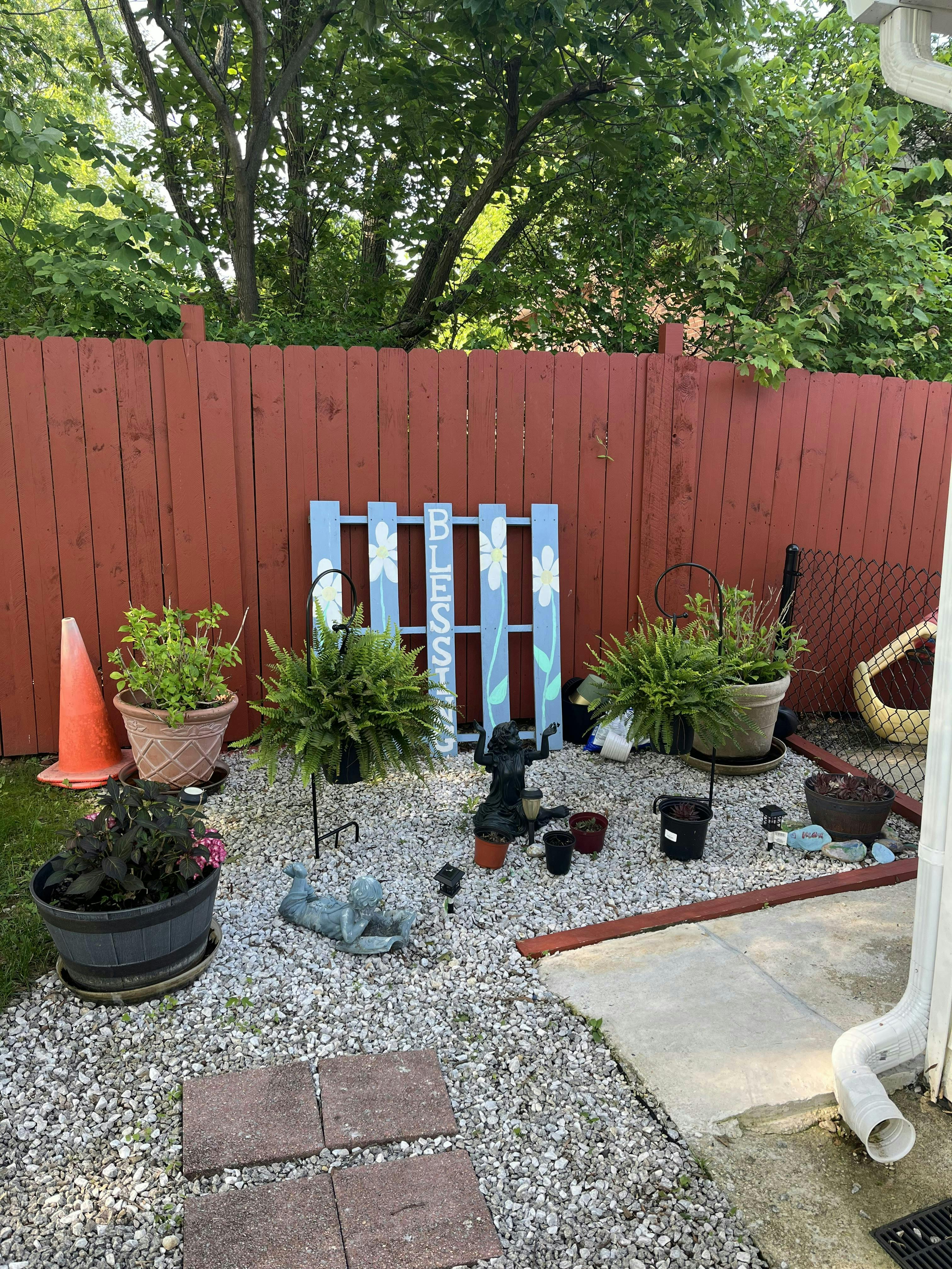 Garden area with potted plants, a red fence, and a blue sign that says "BLESS"