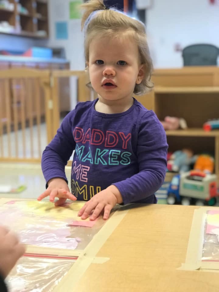 Child standing at a table with hands on a clear plastic sheet
