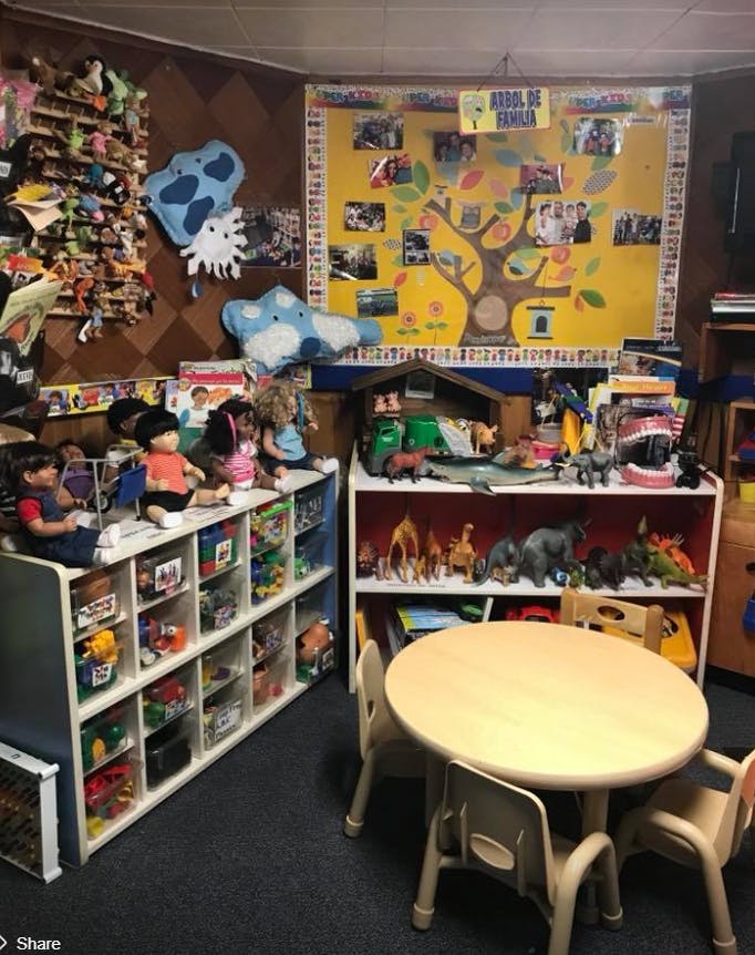 Classroom with shelves of toys, a small table with chairs, and a family tree poster