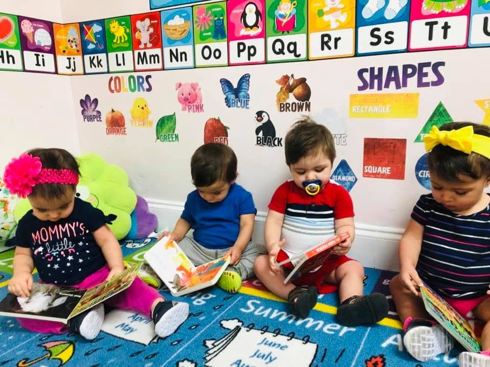 Four young children sitting on a rug, looking at books in a classroom