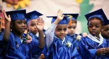 Children in graduation caps and gowns raising their hands