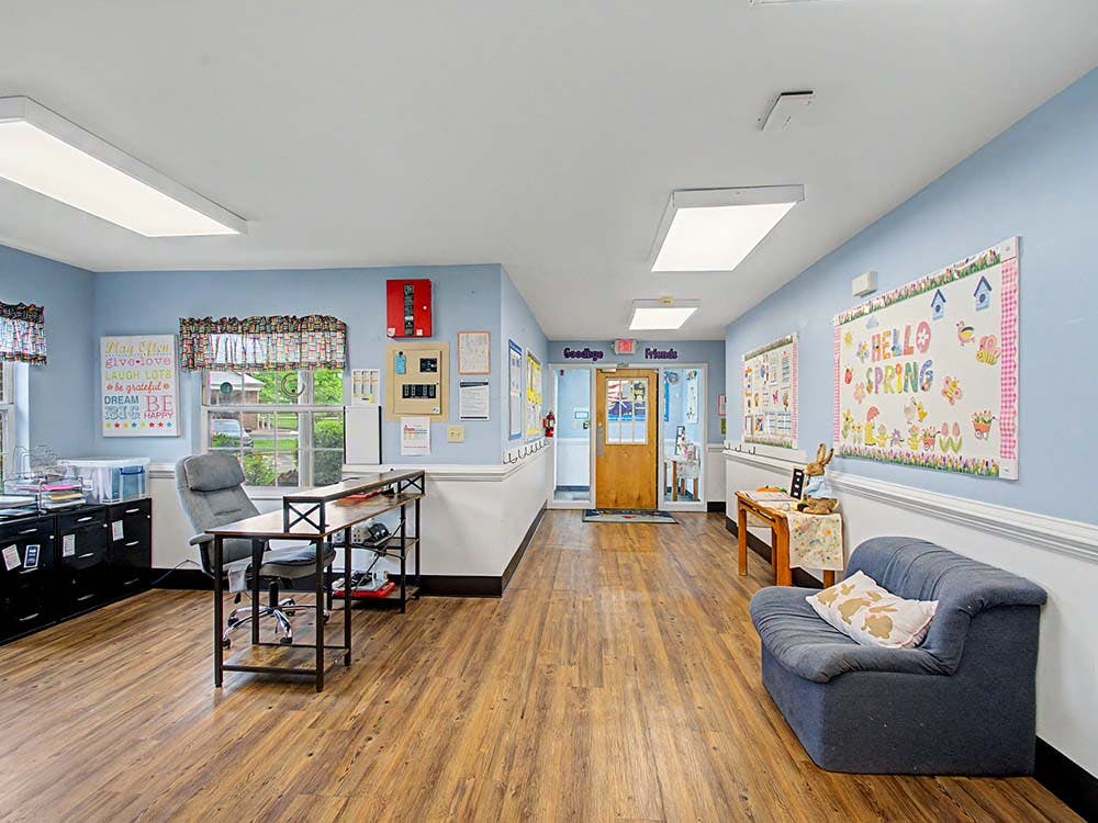 A hallway in a classroom or daycare with a desk, couch, and "Hello Spring" sign