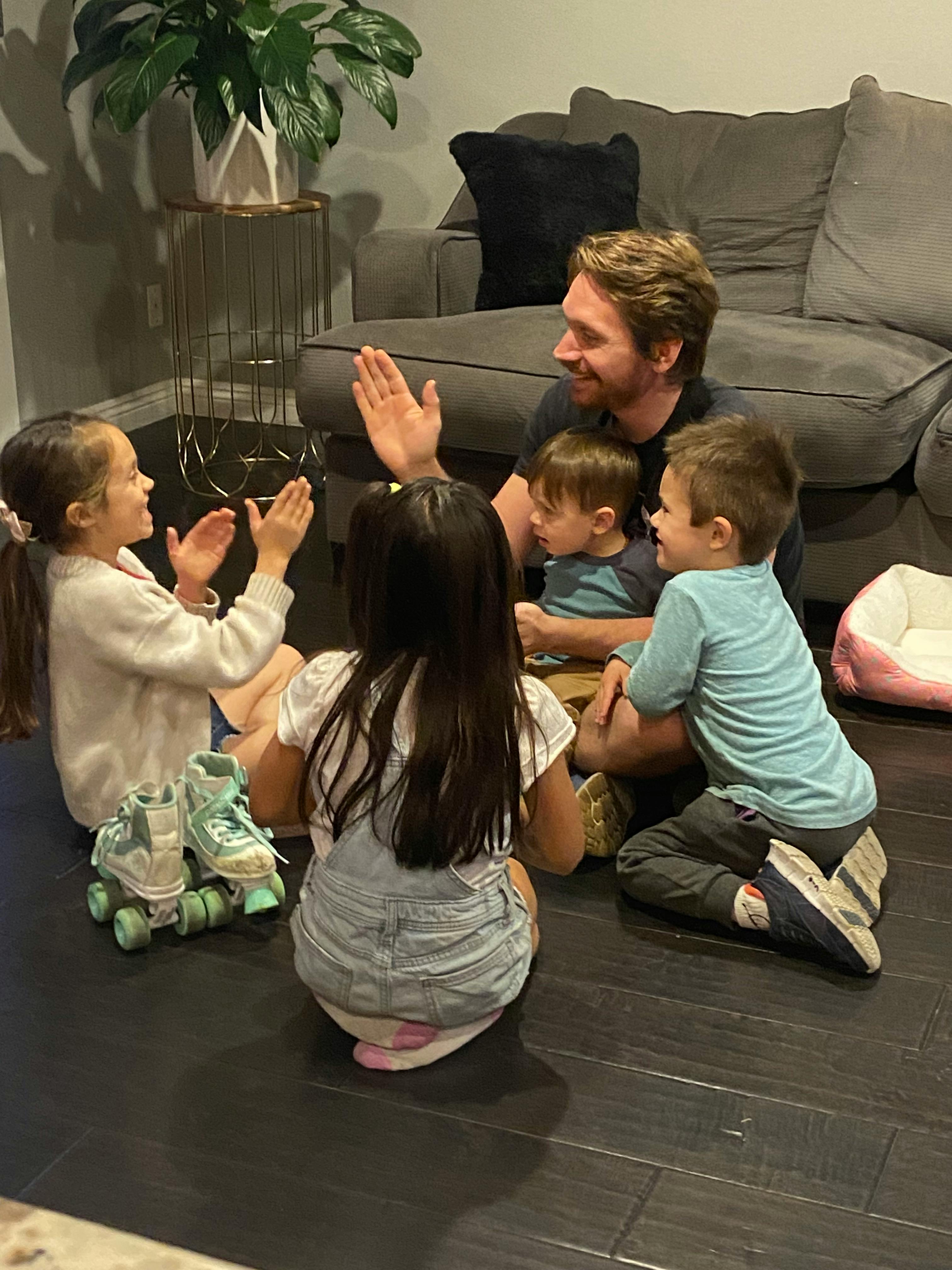 Adult and three children sitting on floor, playing a clapping game