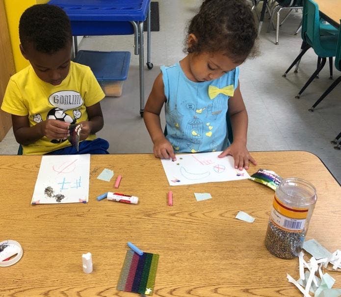 Two children sitting at a table doing crafts in-class activities