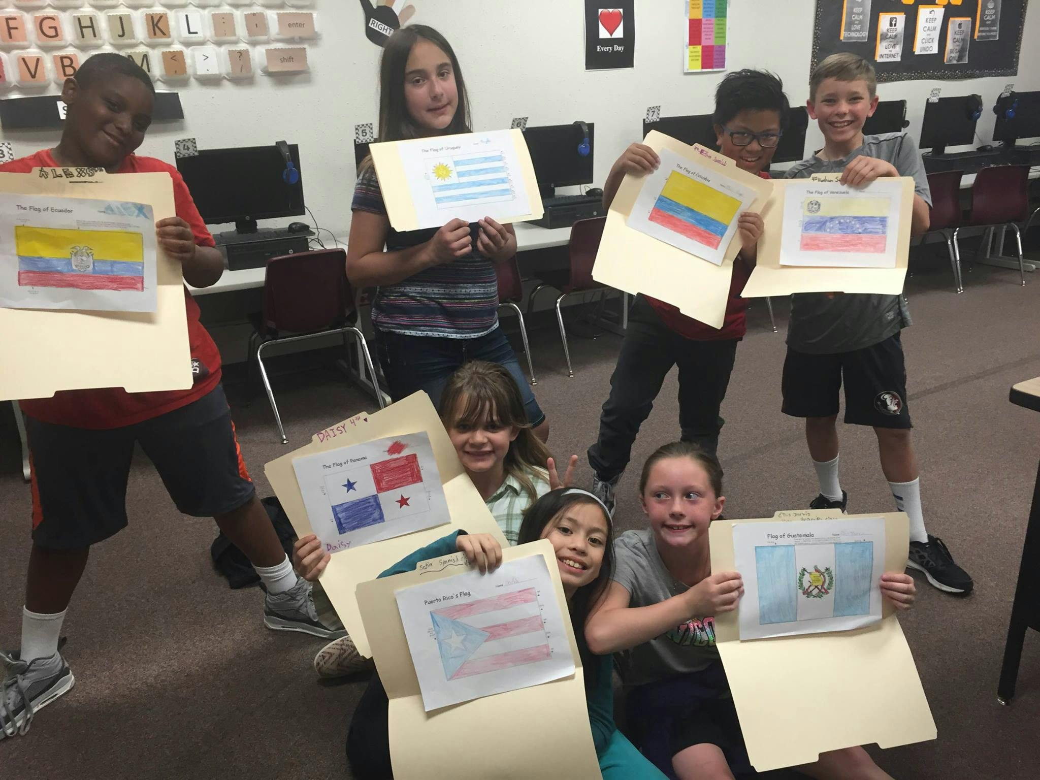 Group of children holding up drawings of flags in a classroom