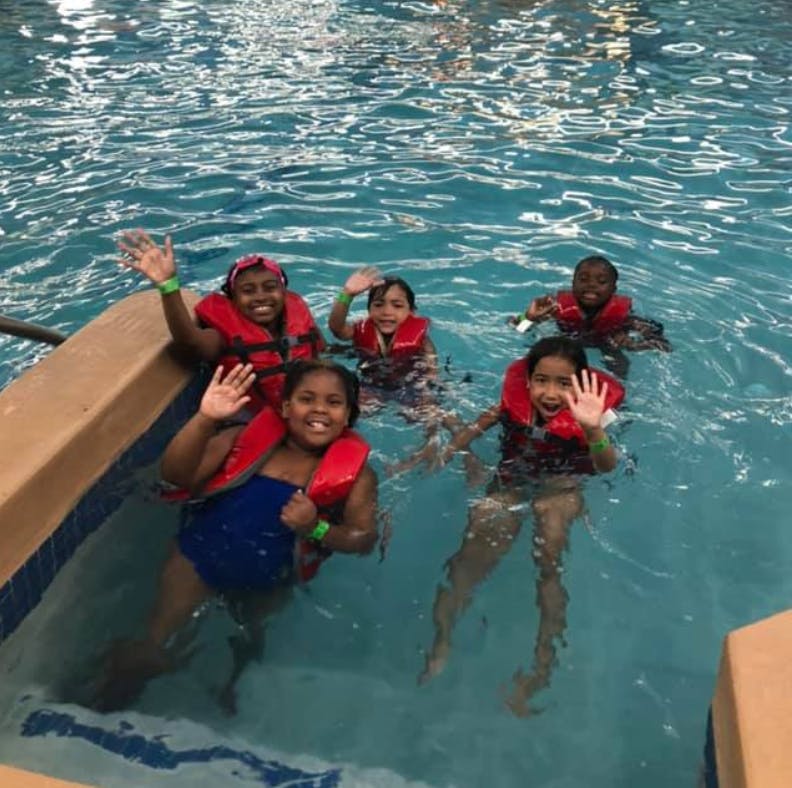 Five children wearing life vests waving in a swimming pool