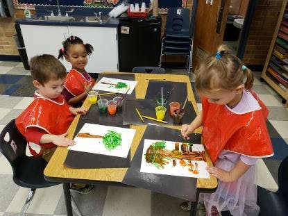 Three children painting at a table in a classroom