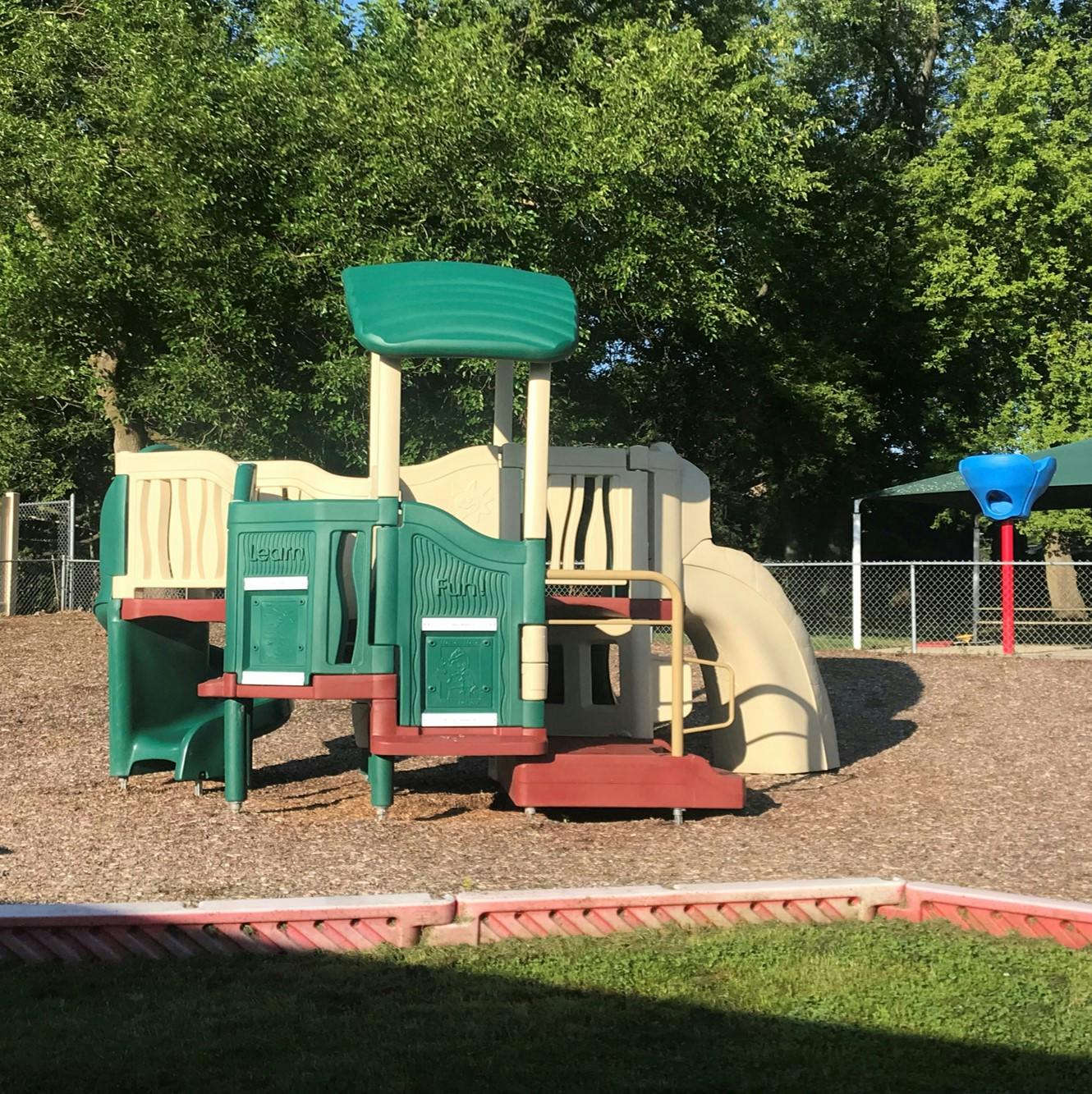 A playground with a slide, climbing structure, and wood chips on the ground