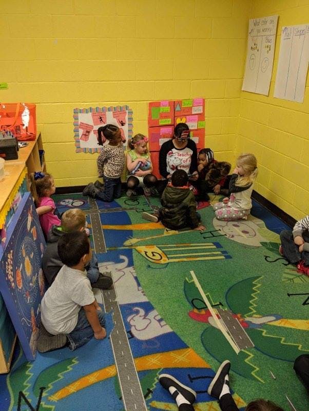 Adult and children sitting on a rug in a classroom