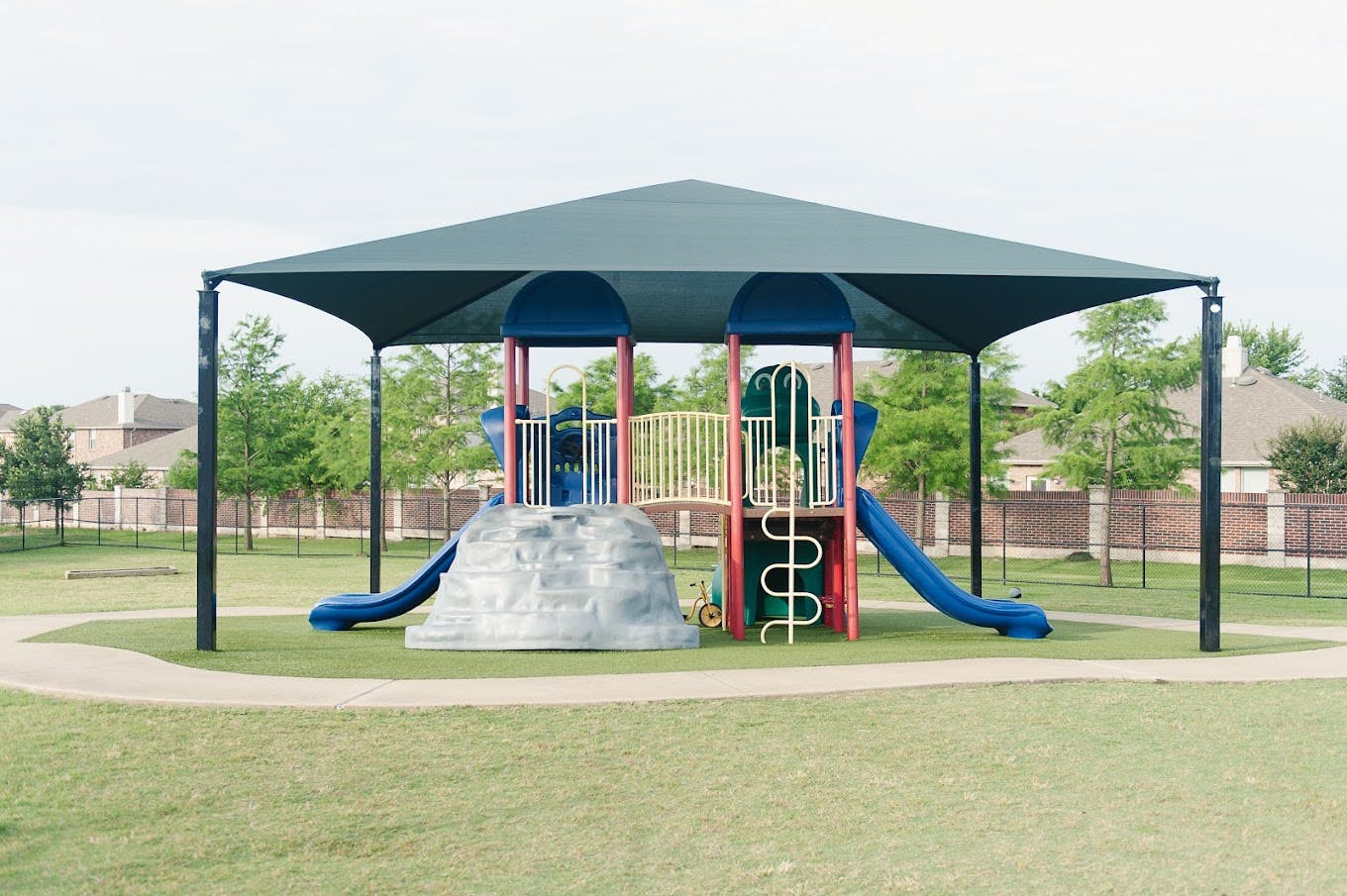 Playground equipment with slides and climbing features under a shade canopy