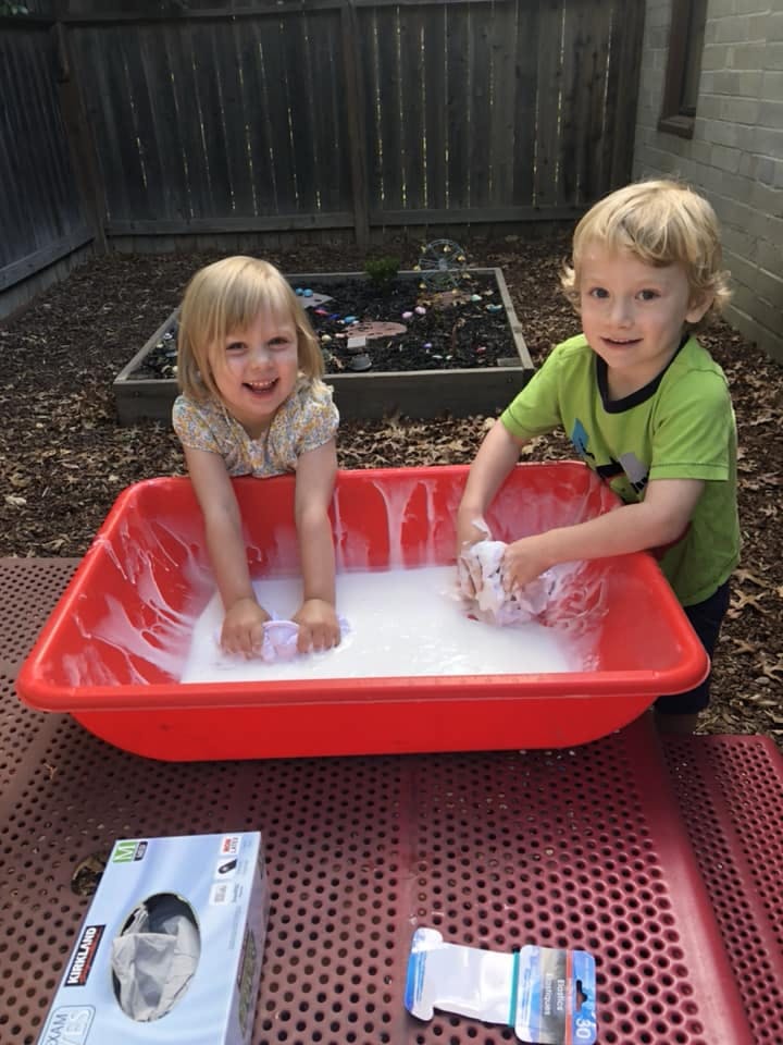 Two children playing in a red tub filled with soapy water