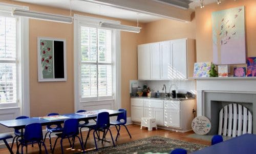 Classroom with blue tables and chairs, white cabinets, and a fireplace