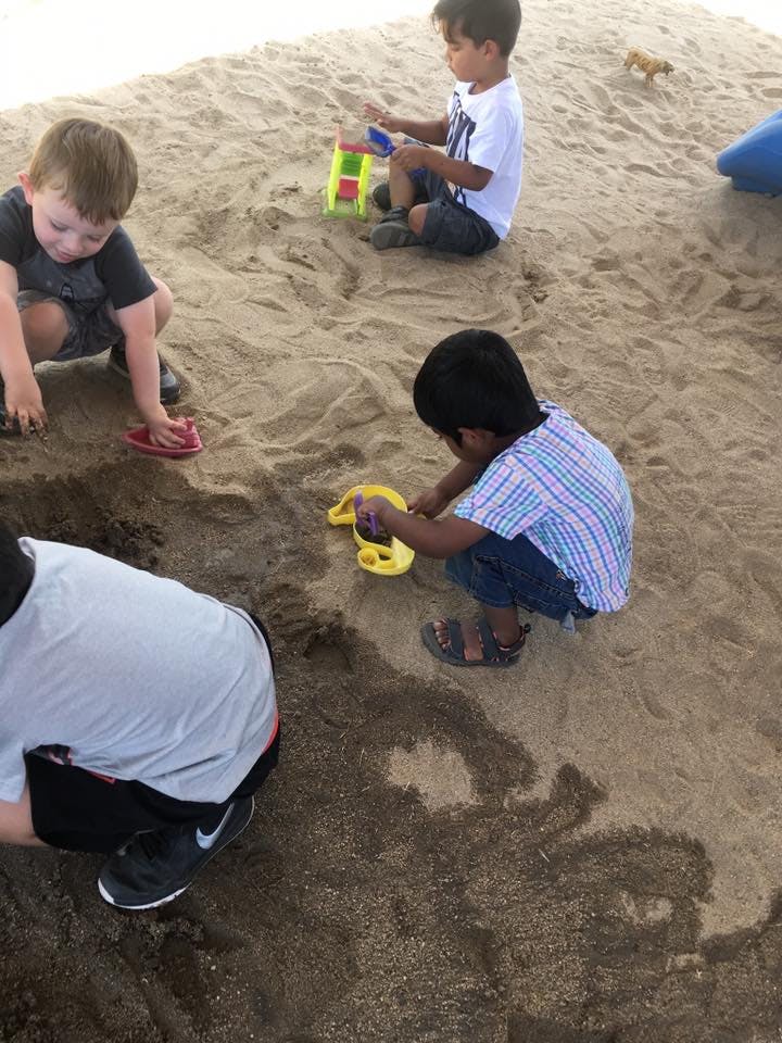Three children playing in sand with sand and toys
