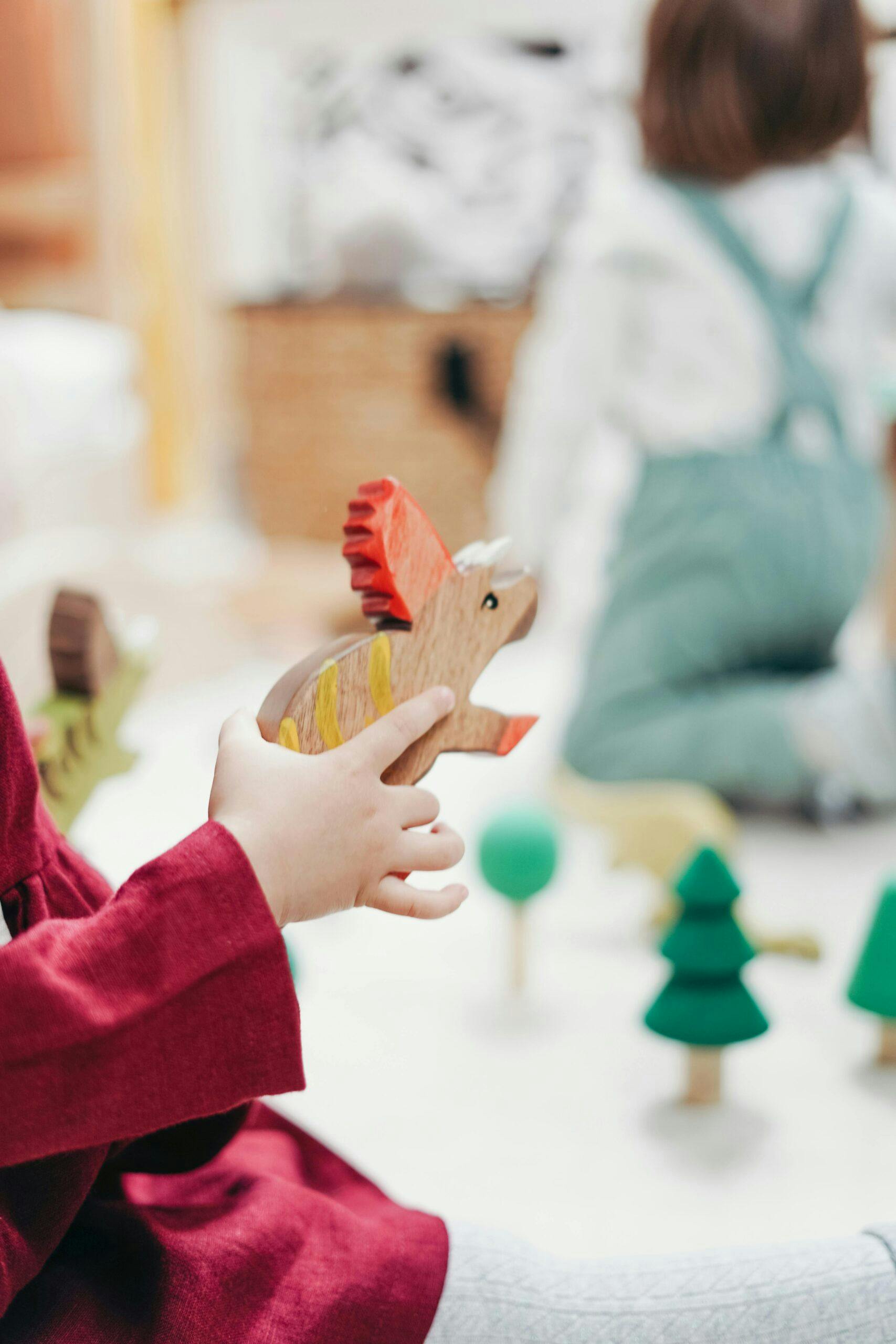 Child in red top playing with a wooden dinosaur toy