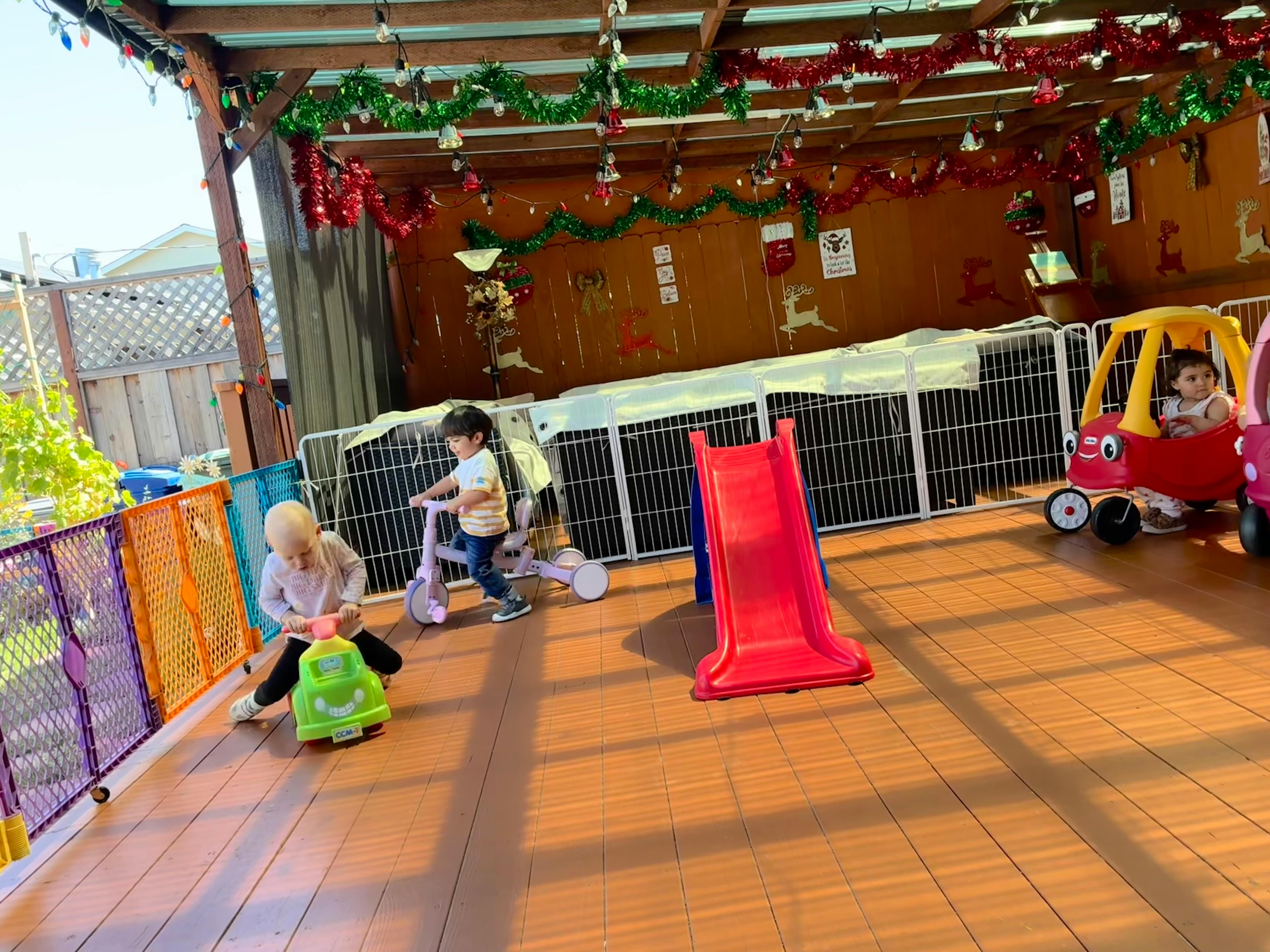 Three children playing with toy vehicles and a slide on a wooden deck