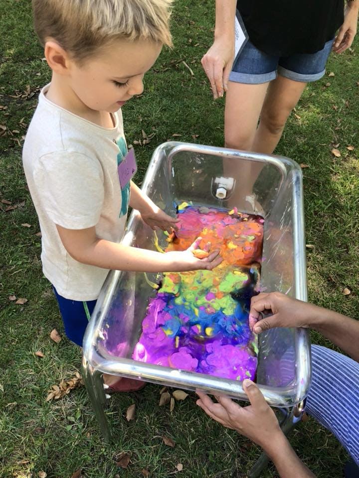 Child playing with colorful slime in a metal bin outdoors