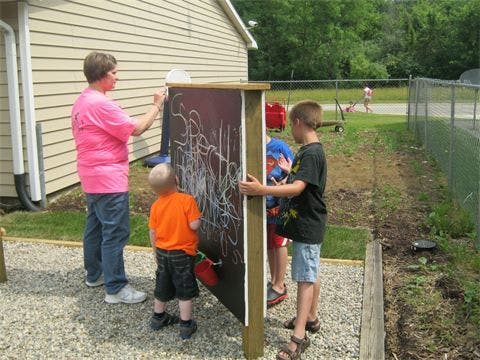 Adult and children drawing on a chalkboard outdoors