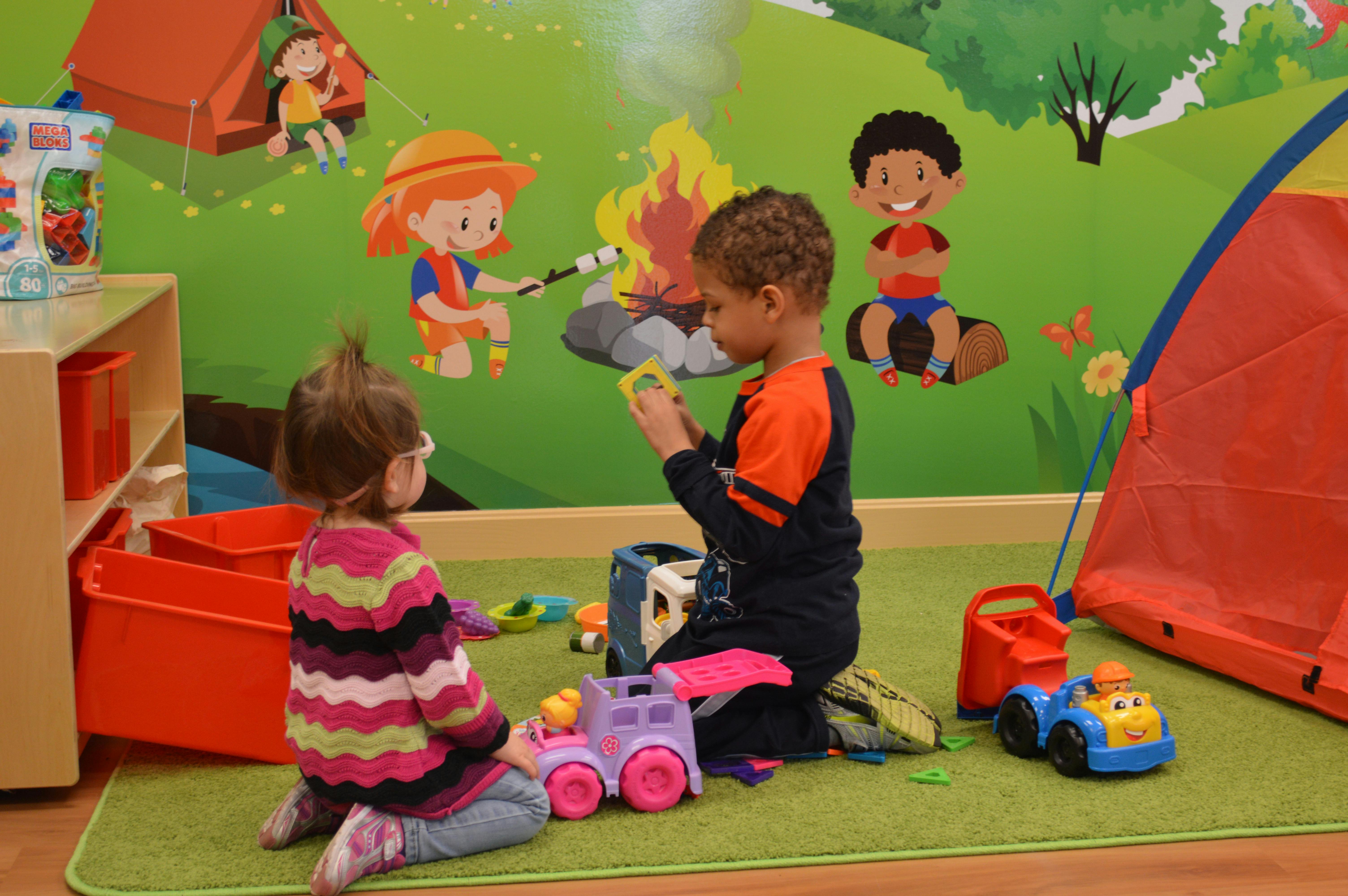 Two children playing with toys on a green mat