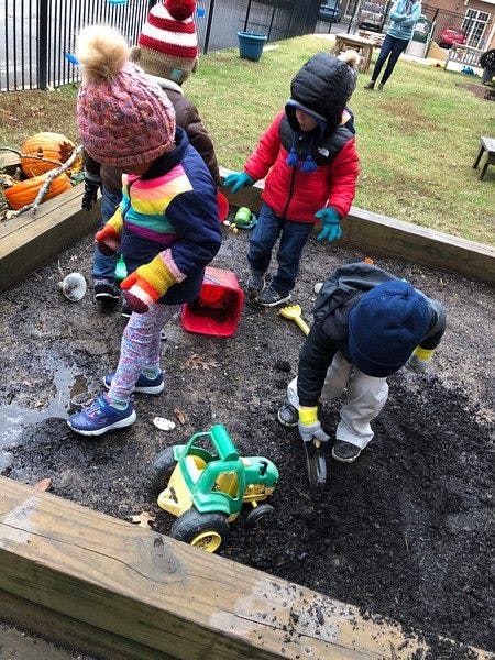 Children playing in a sandbox with dirt and toys