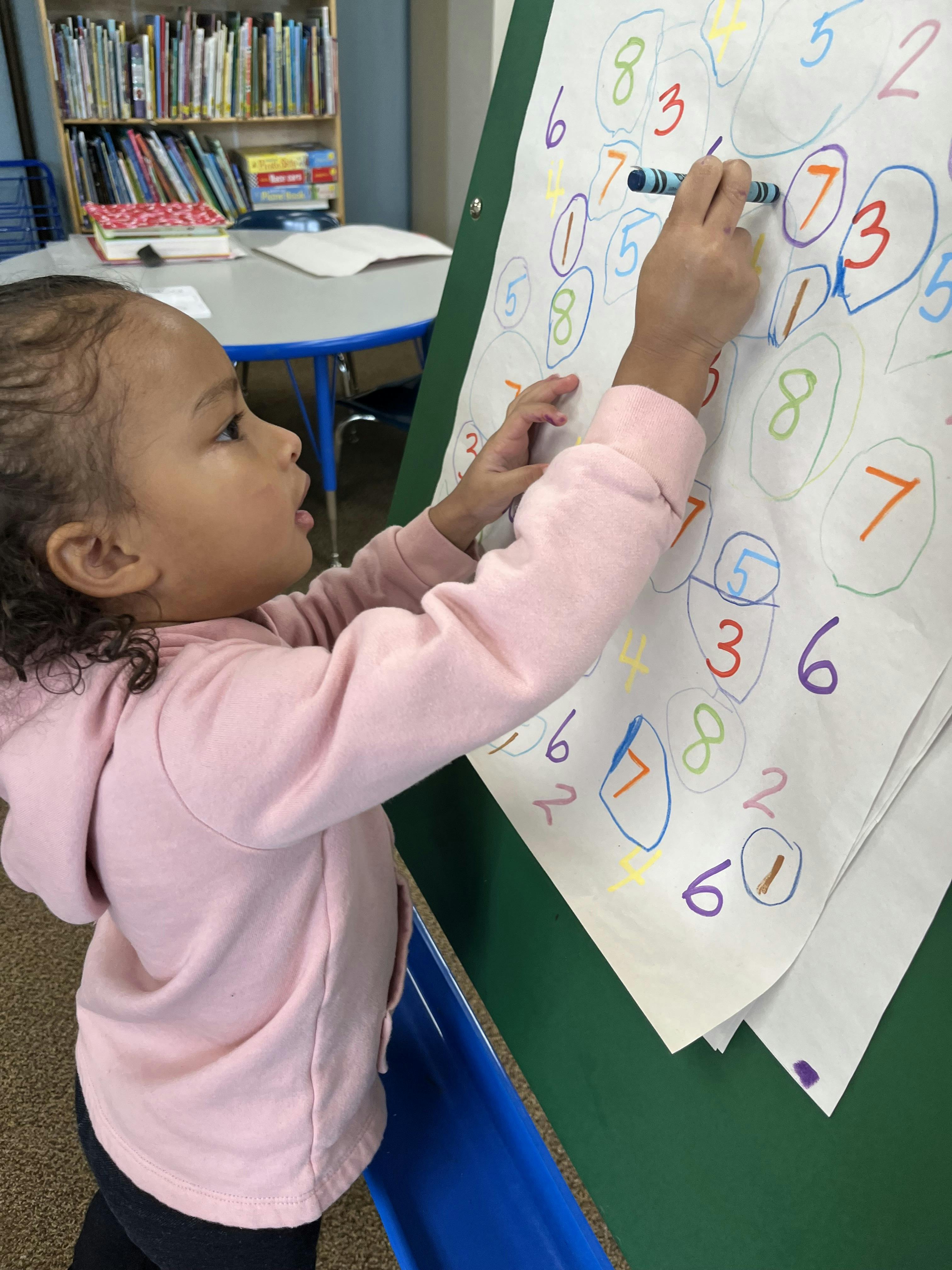 Child drawing numbers on a large paper with a crayon