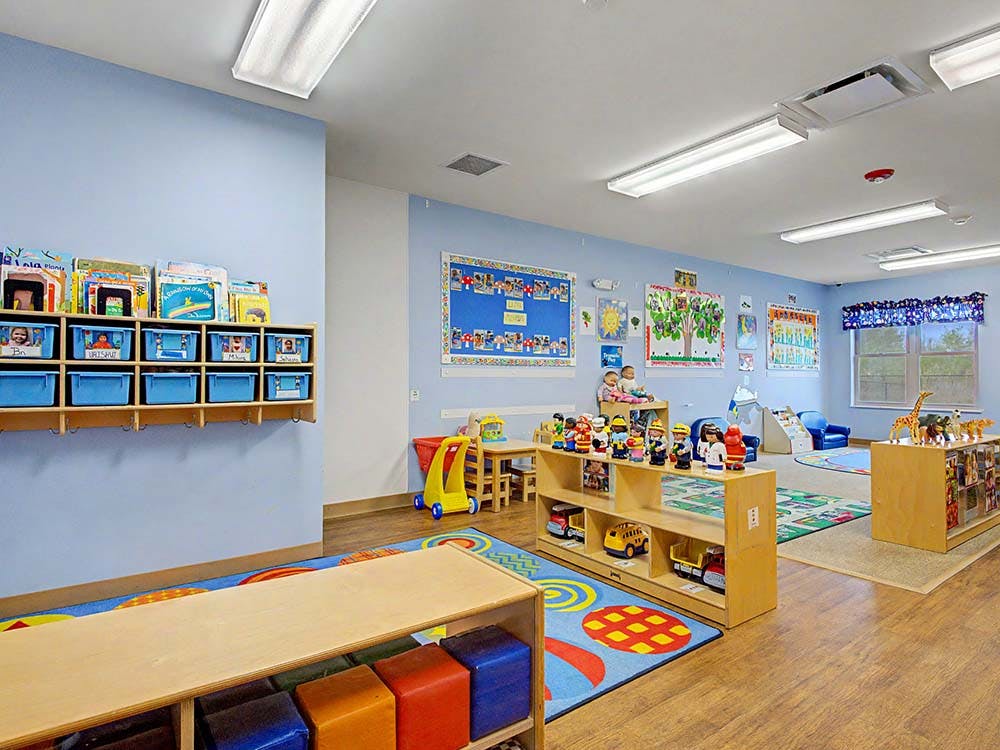 Classroom with light blue walls, shelves of books and toys, and a colorful rug