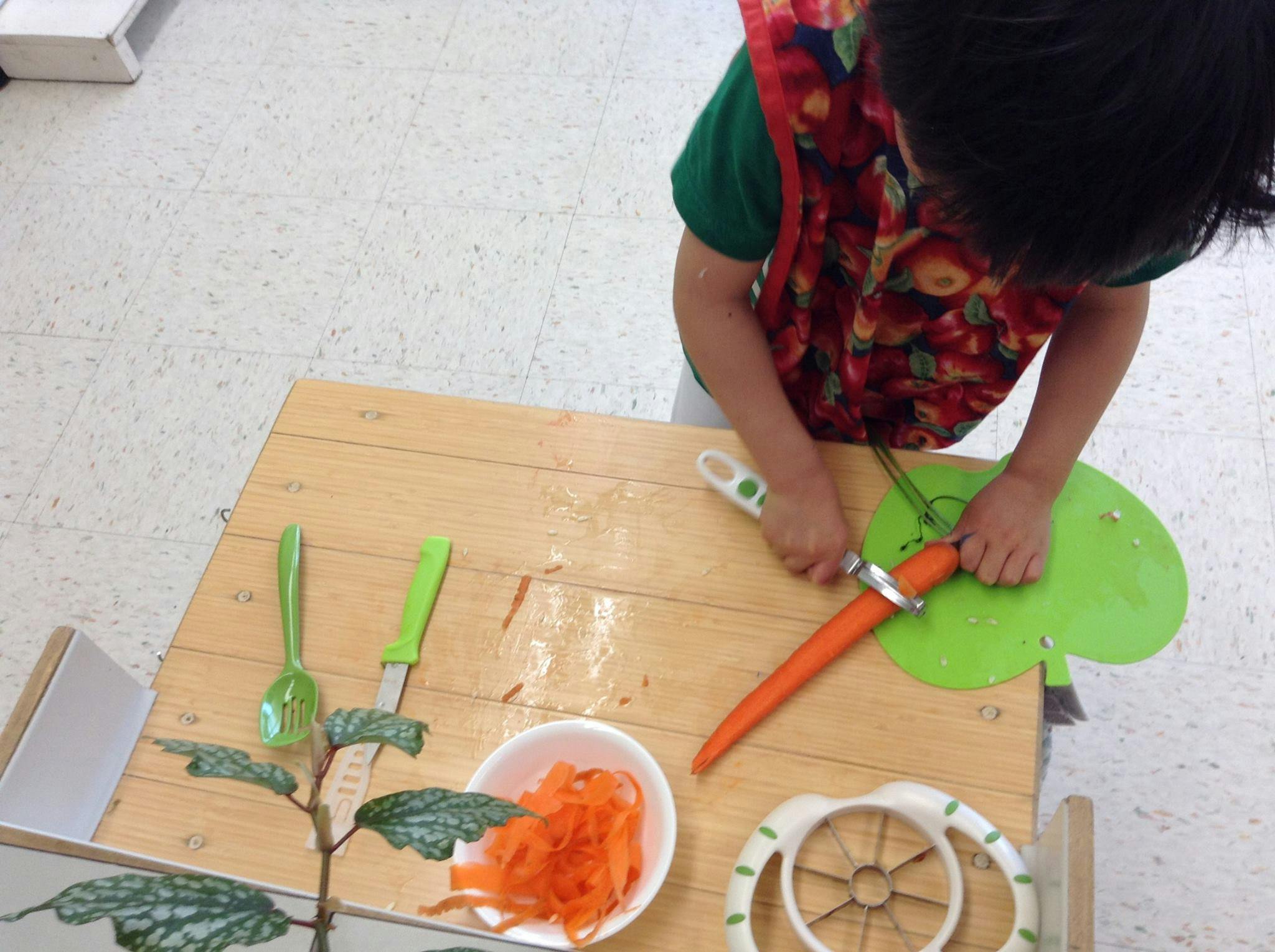 Child cutting a carrot on a green cutting board