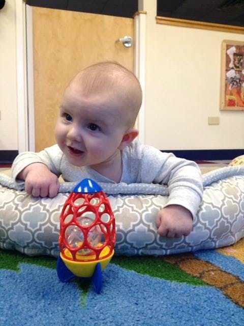 Child on stomach looking at a rocket toy