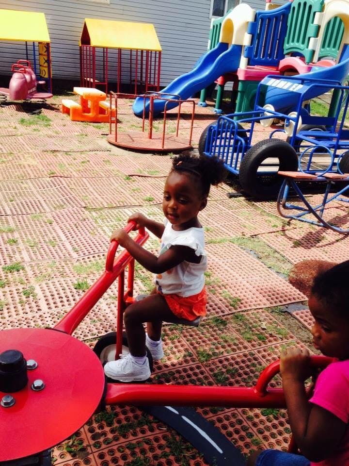 Child on a red playground ride with another child nearby