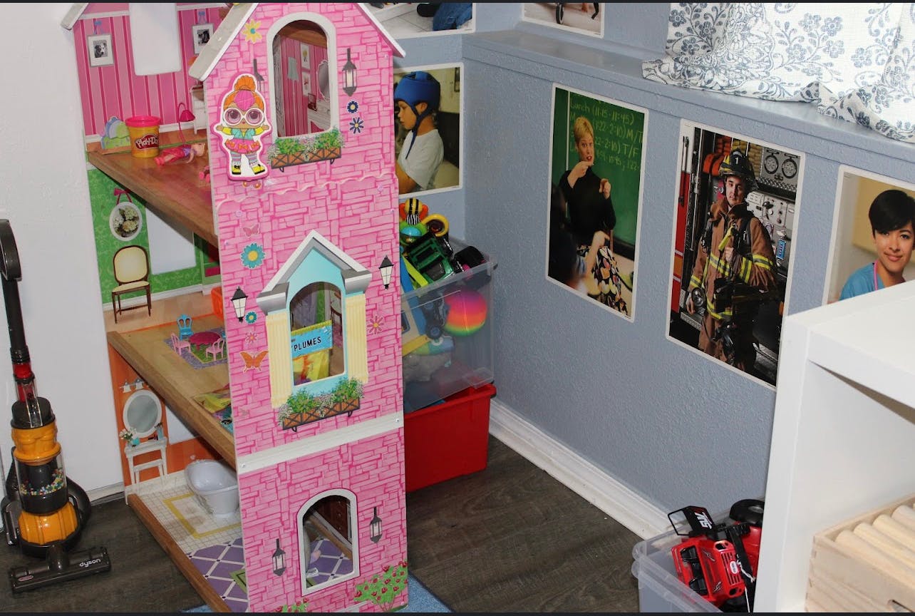 Pink dollhouse next to a vacuum cleaner and posters on a wall
