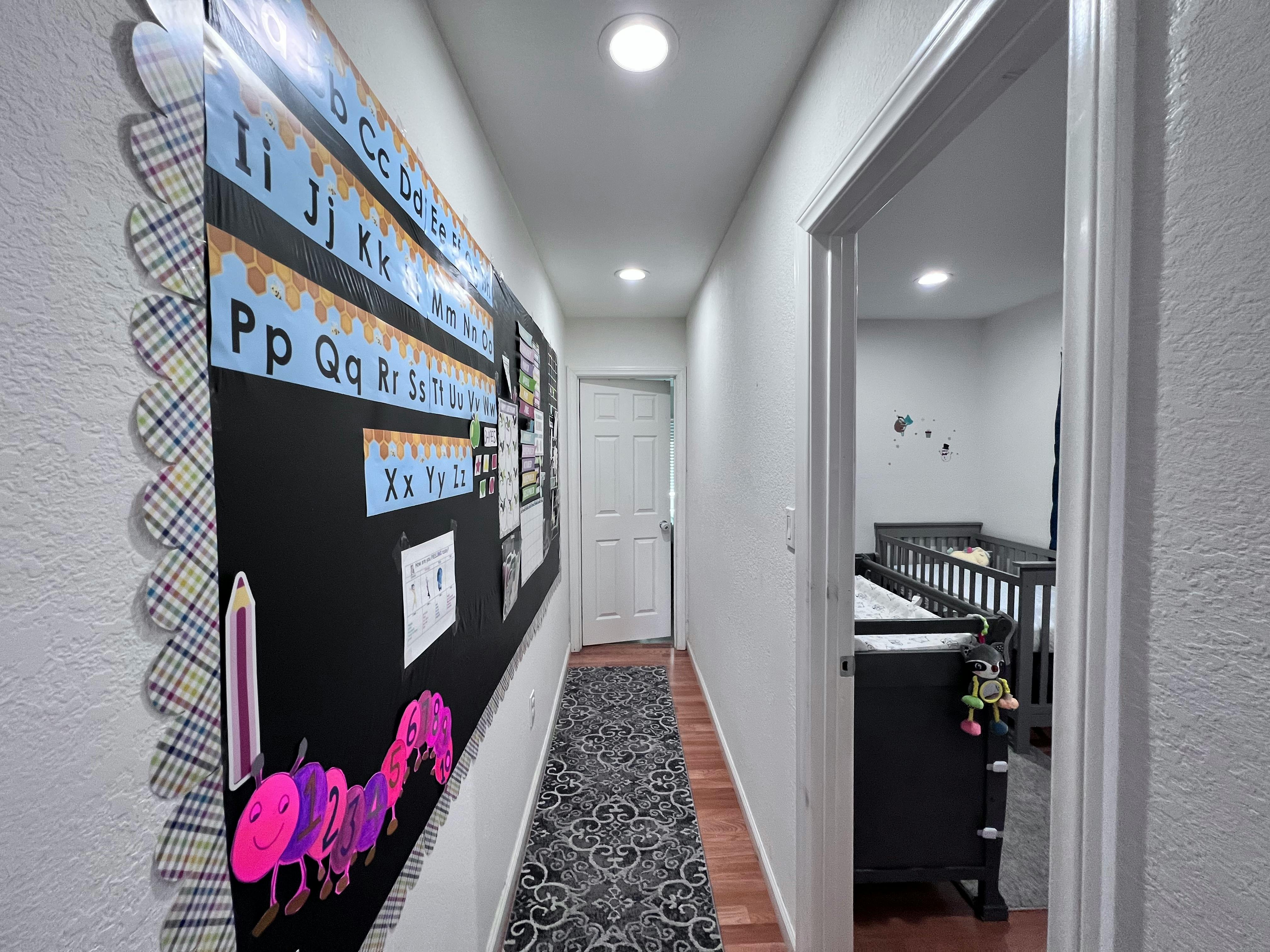 Hallway with a bulletin board displaying alphabet letters and a nursery visible through an open door