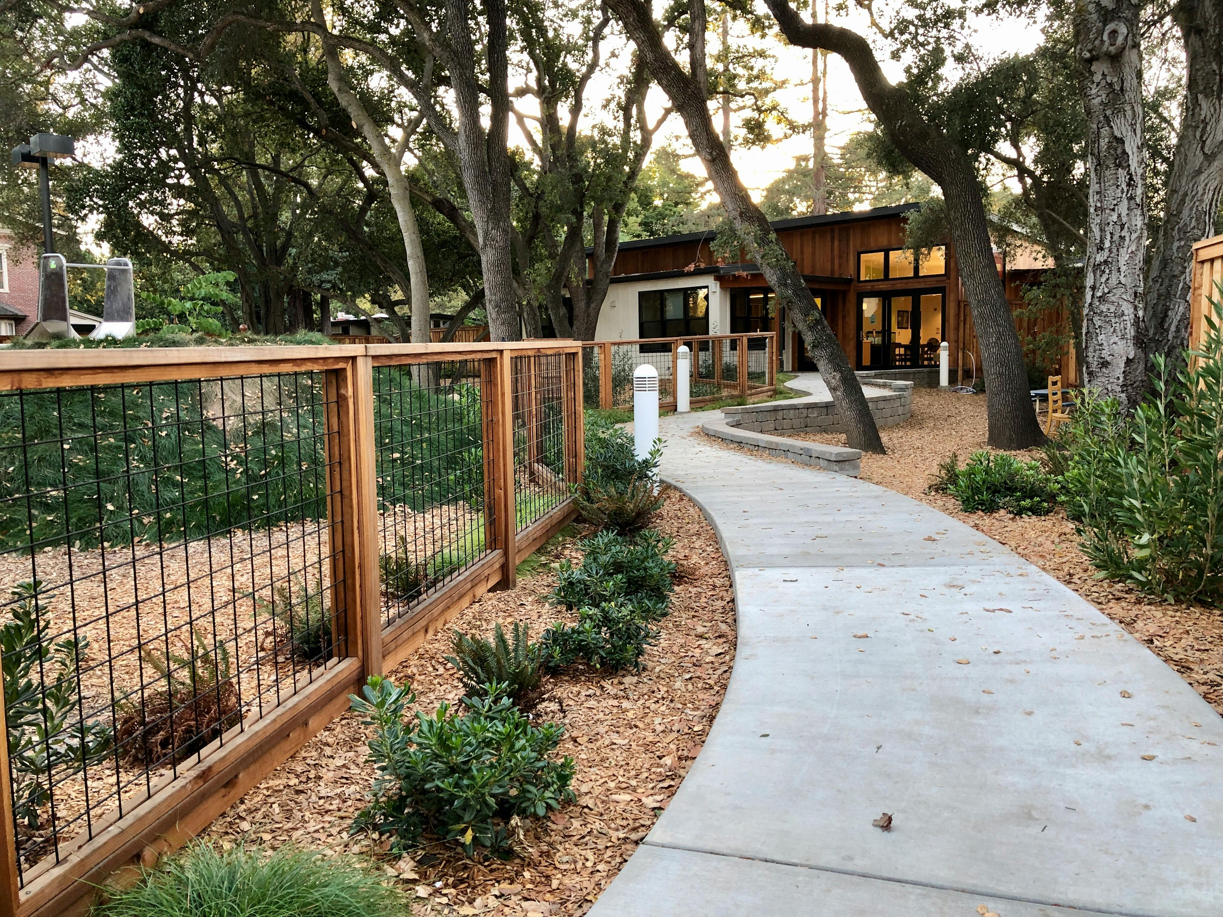 Curved concrete path leading to a building with a wooden fence and trees