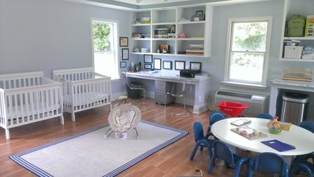 Two cribs, a small table with chairs, and a desk in a room