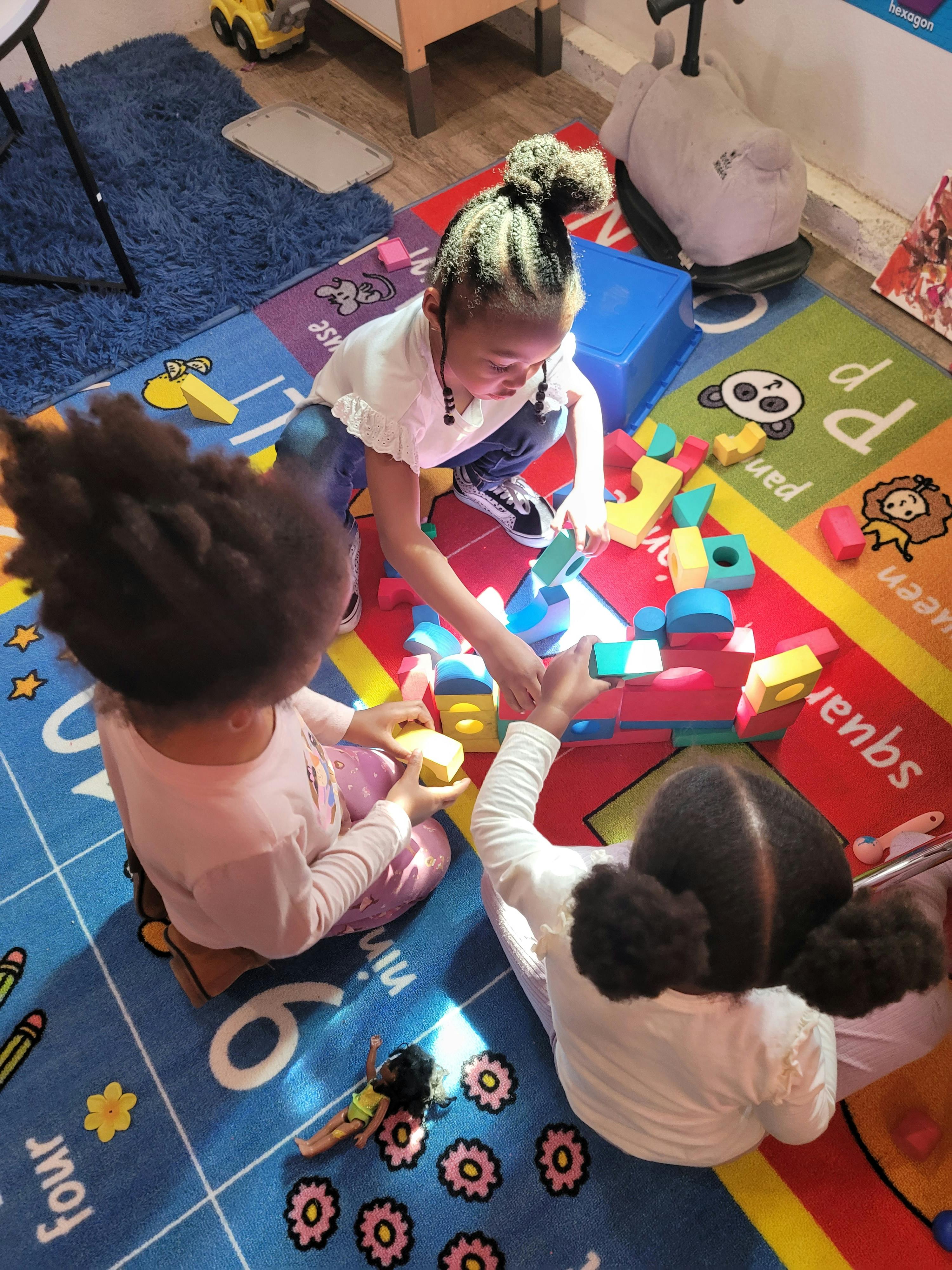 Three children playing with colorful building blocks on a rug