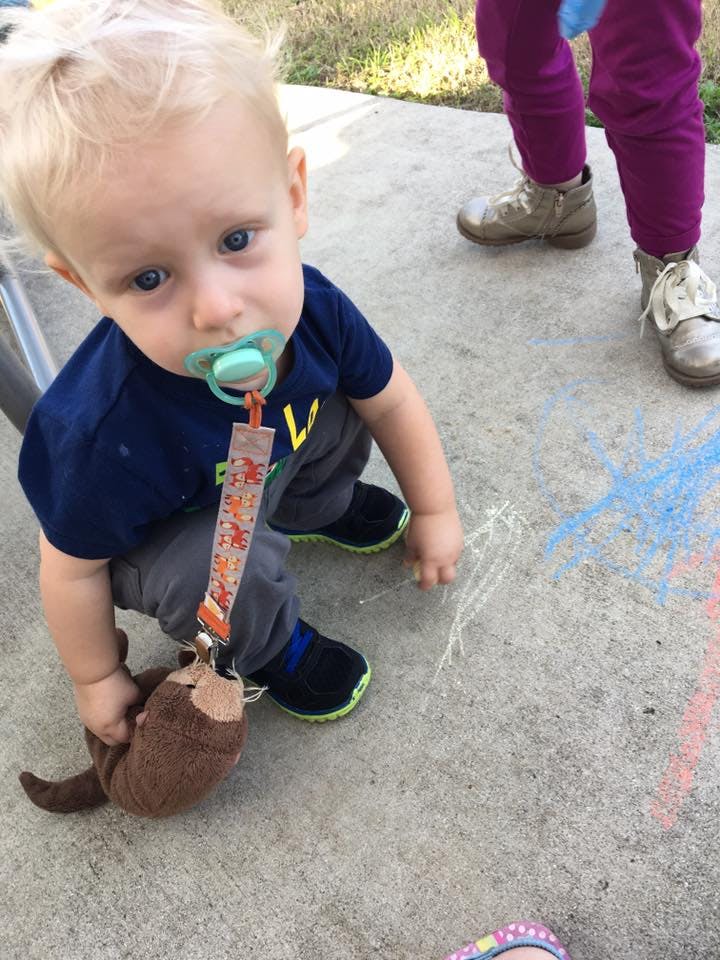 Child with pacifier and stuffed animal on concrete with chalk drawings