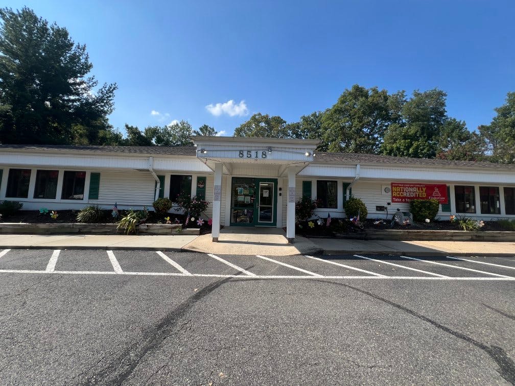 A low, white building with green shutters and "8518" above the entrance