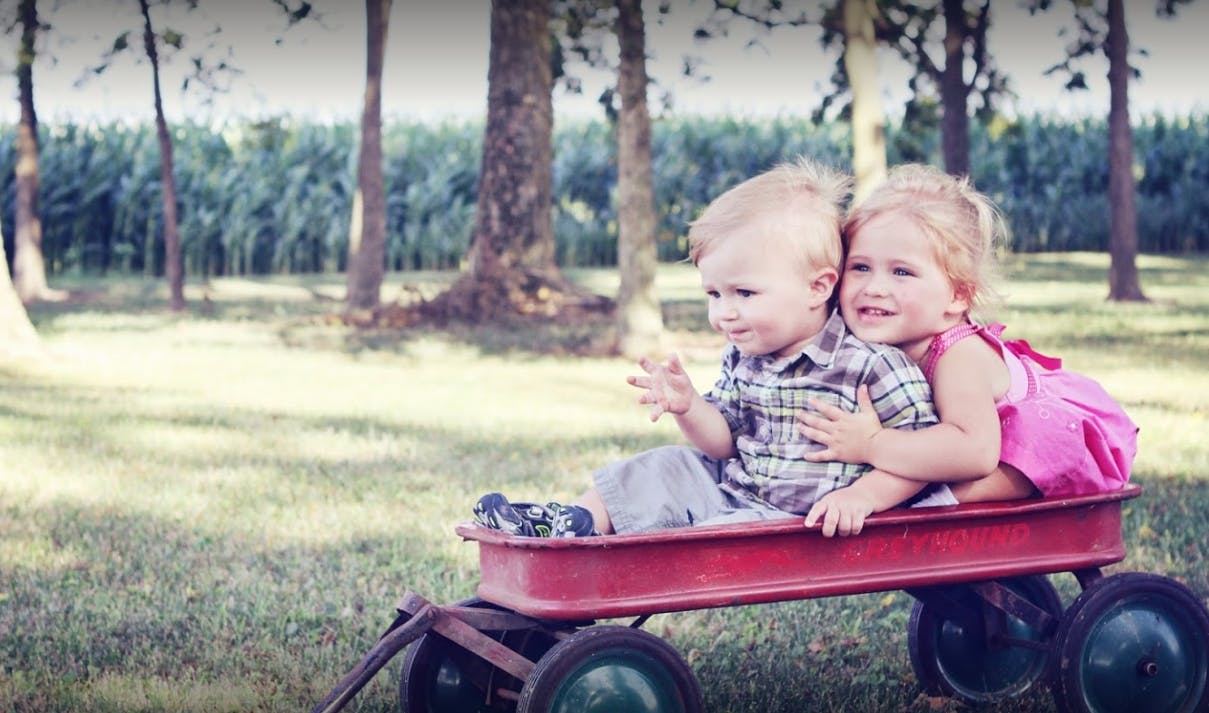 Two children sitting in a red wagon outdoors