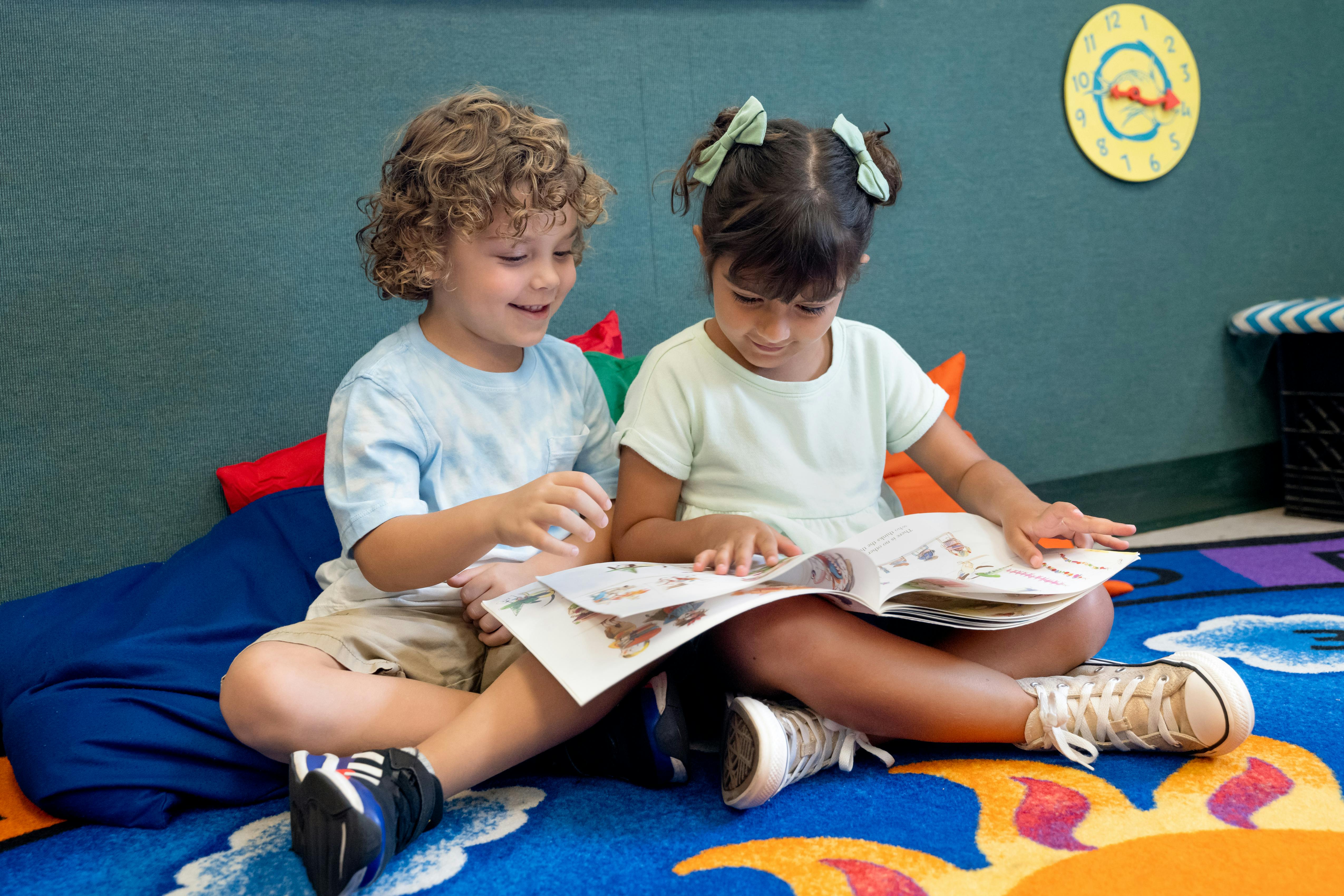Two children sitting on a rug and reading a book together
