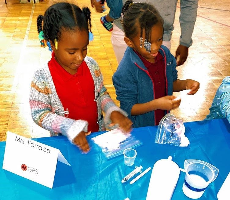 Two children at a table with various items, one child looking down at the table