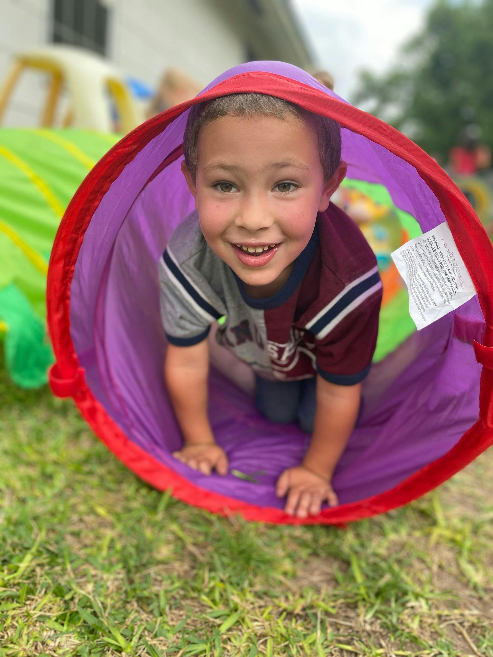 Child crawling through a purple play tunnel on grass