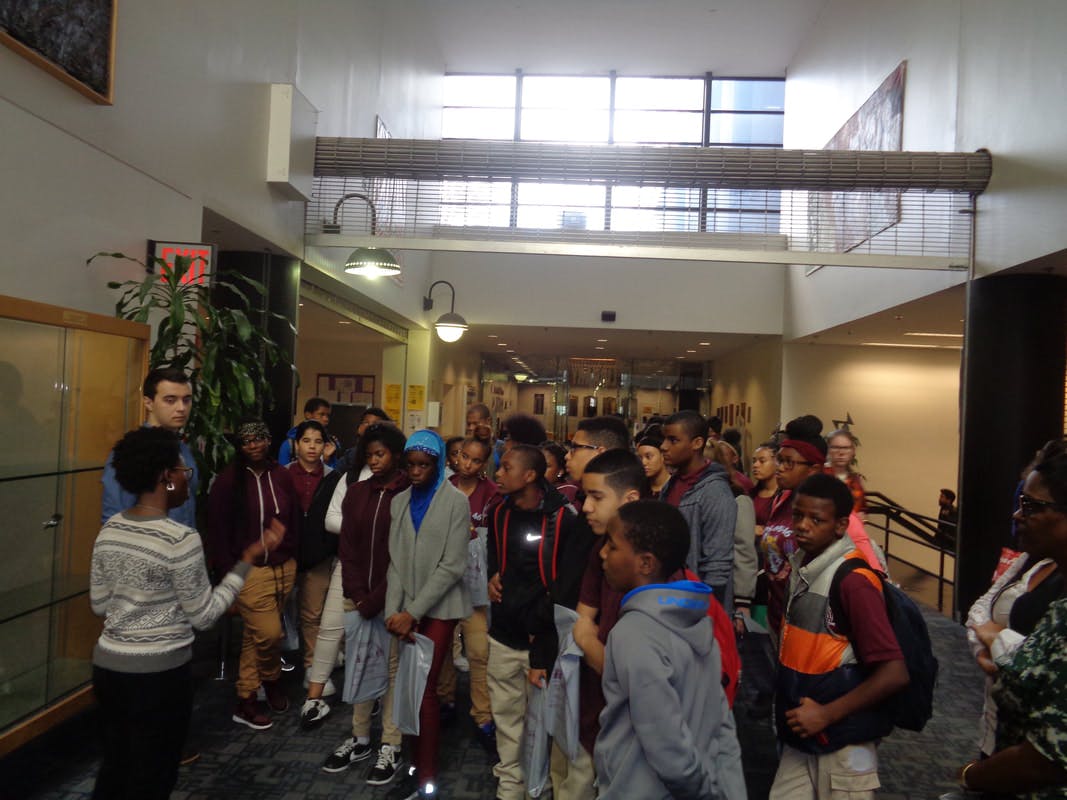 Person speaking to a group of teens in a hallway