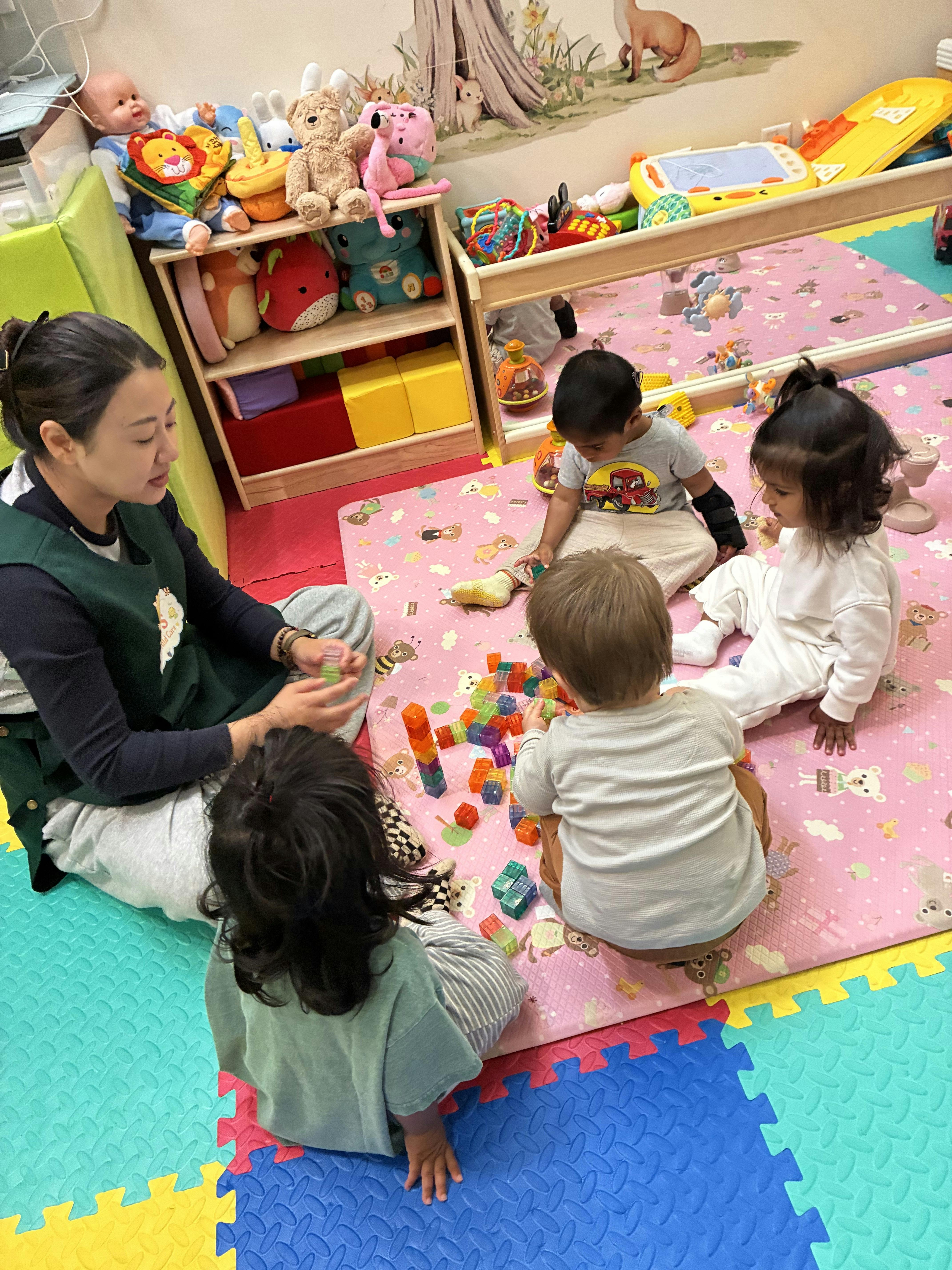 Adult and children playing with plastic building blocks on a colorful play mat
