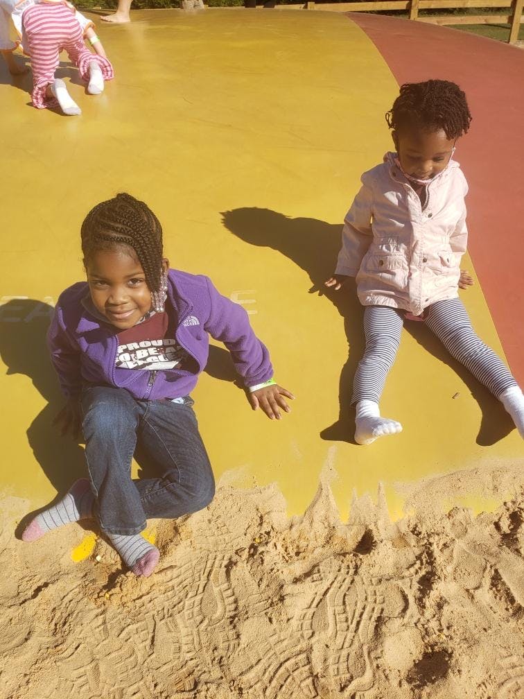 Two children sitting on a yellow surface next to a sand area