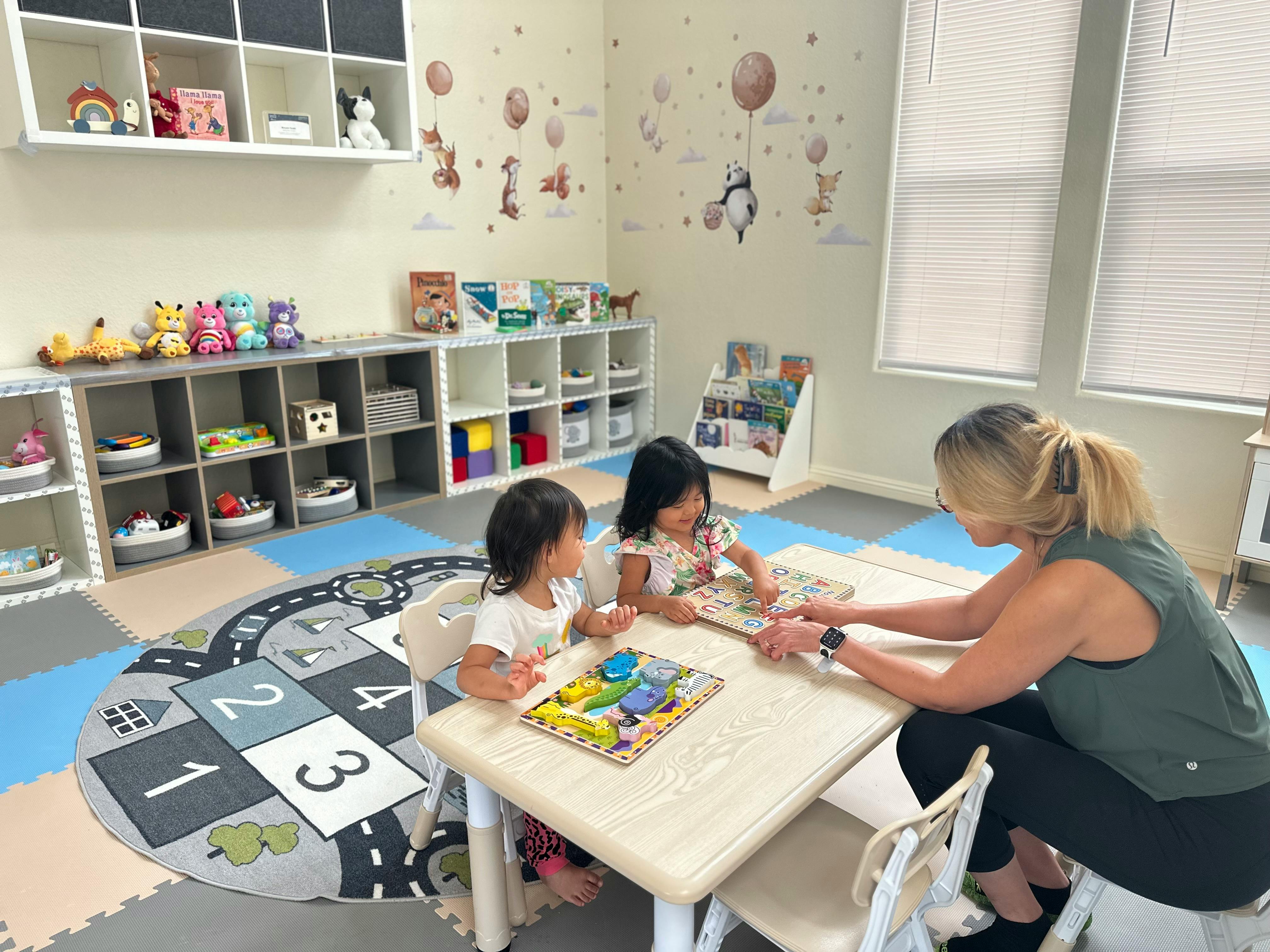 Adult and two children at a table with puzzles in a playroom