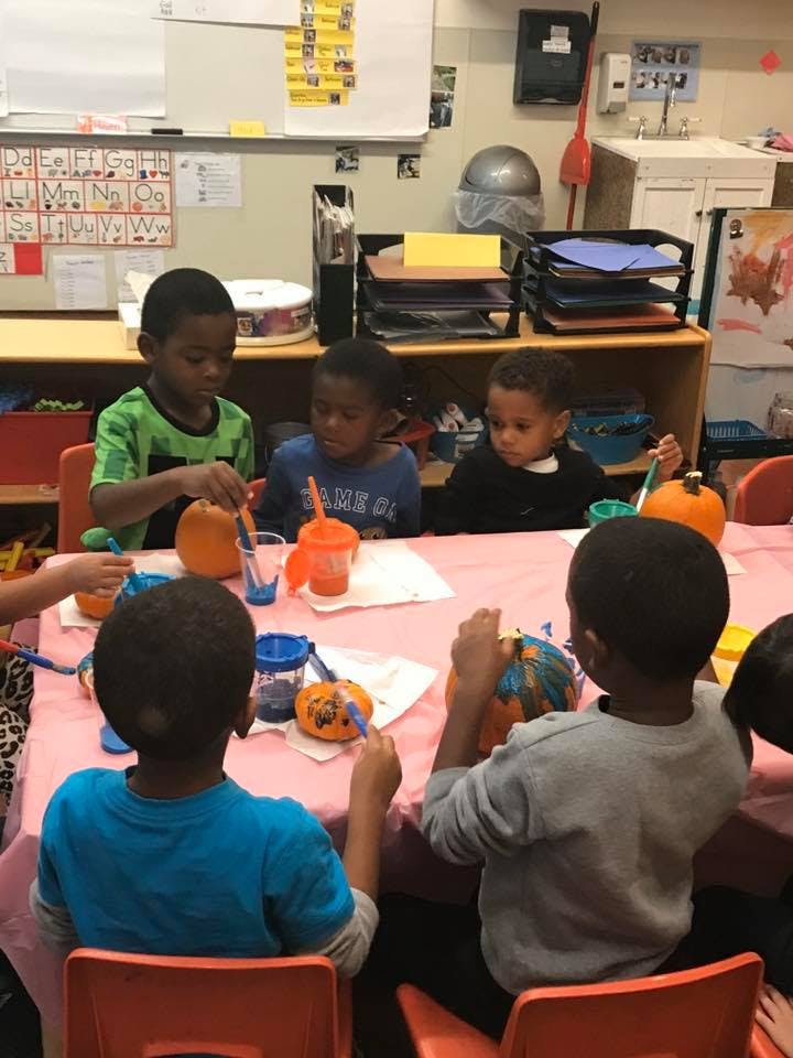 Children painting pumpkins at a table in a classroom