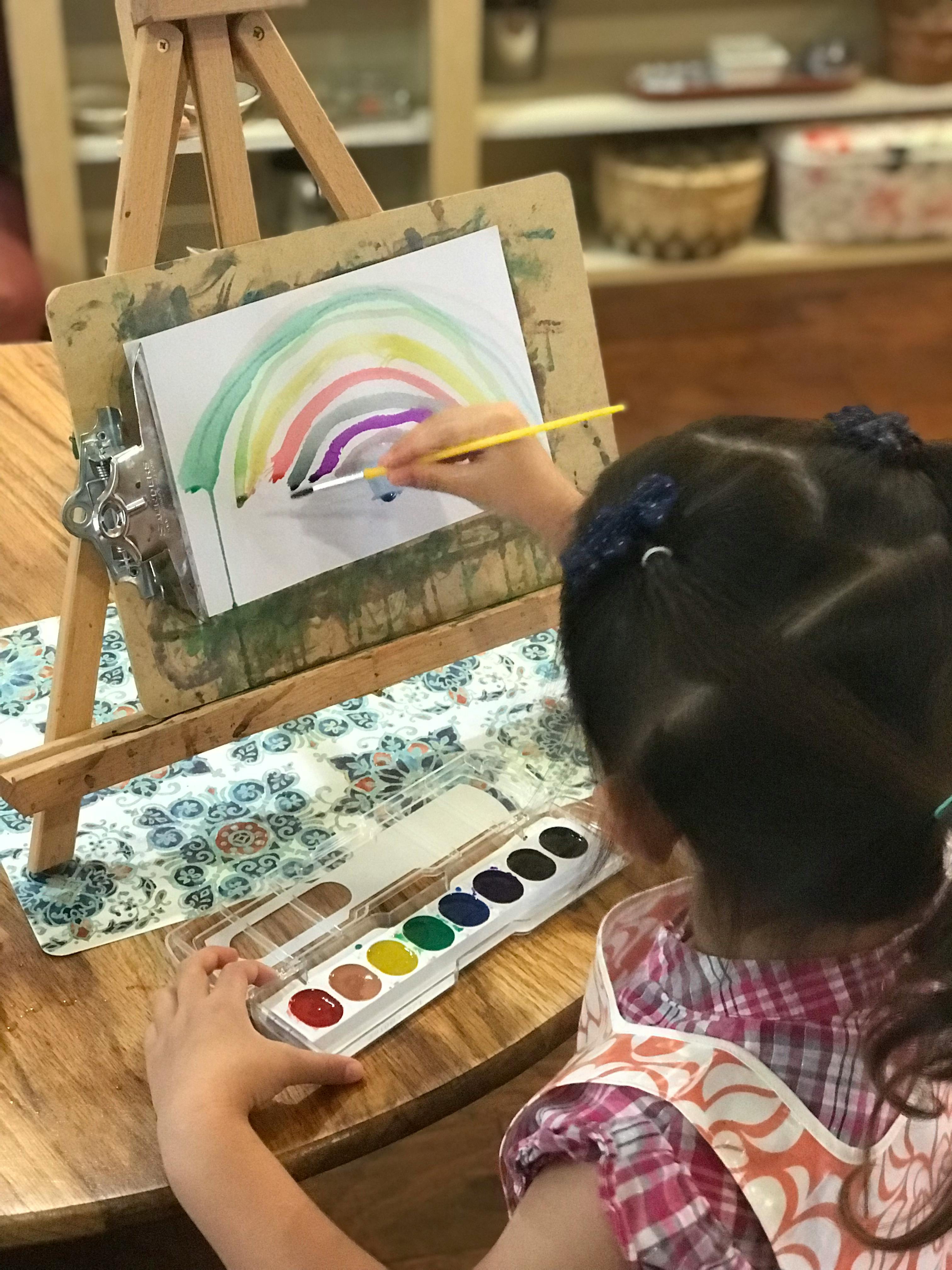 Child painting a rainbow on an easel with watercolors
